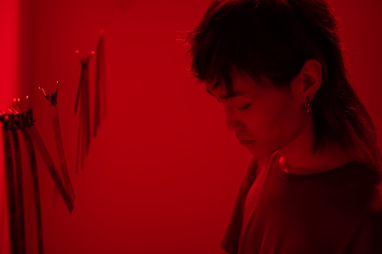 Female photographer working in a red-lit darkroom developing photos.